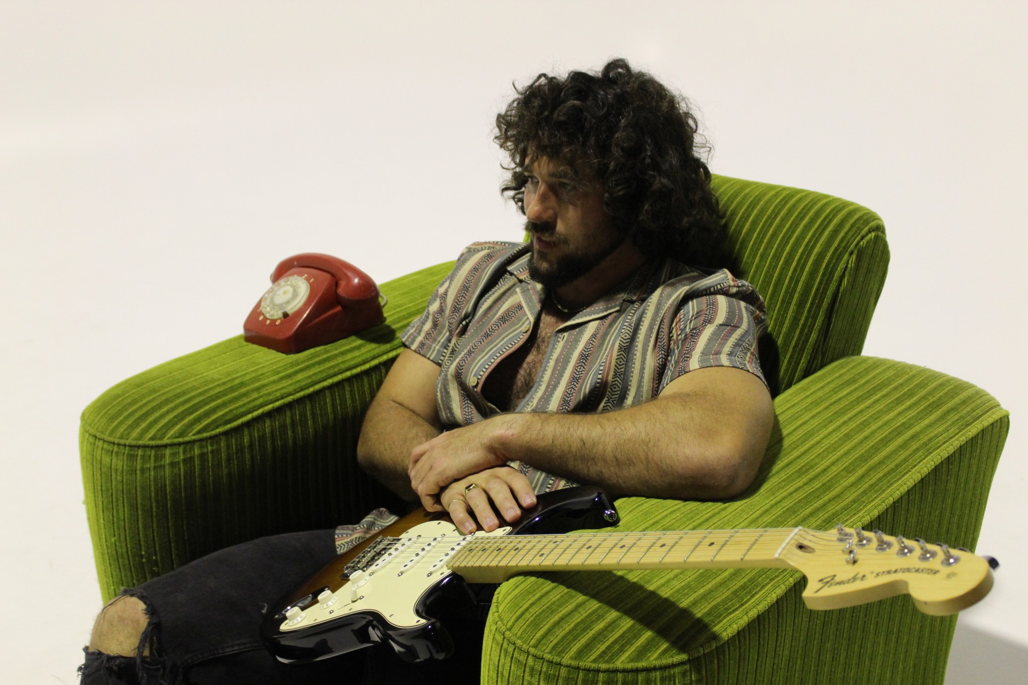 Grant Walker sitting in a green armchair with a Fender Stratocaster